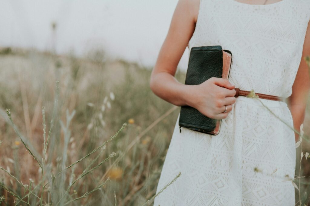 Girl in a field in white dress holding a bible